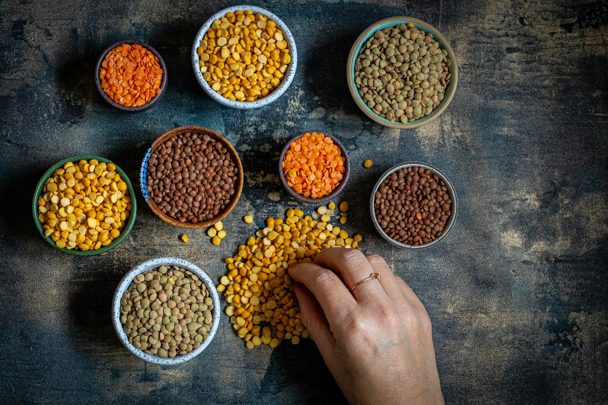 A hand touching a bowl of dry lentils on a table (photo: Monika Borys, Unsplash)